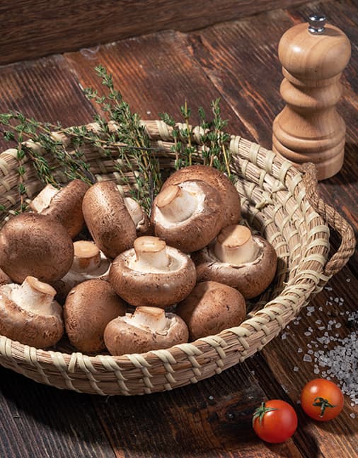 Champiñones Crimini Setas de Cuivá dentro de canasta circular de mimbre acompañado de romero, tomates cherry y sal de mar