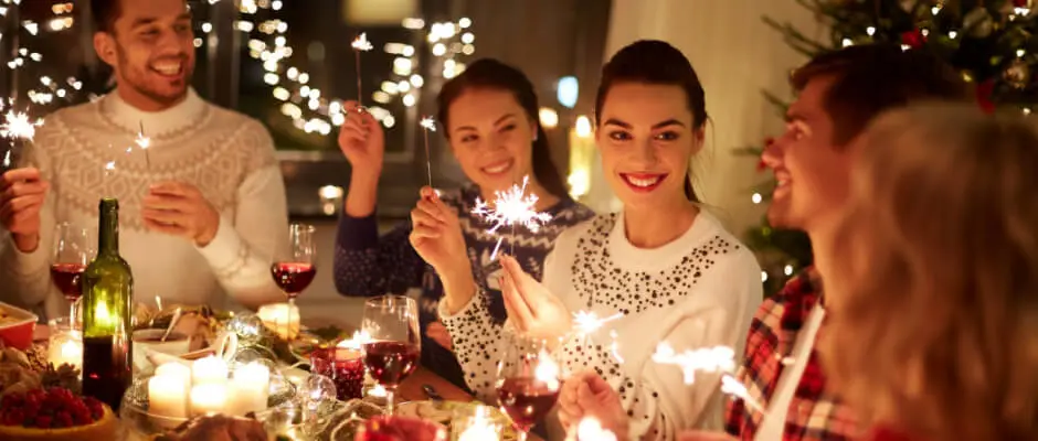 Cena navideña con Setas de Cuivá, velas y copas de vino, las personas sonríen mientras elevan chispas de luces en celebración.
